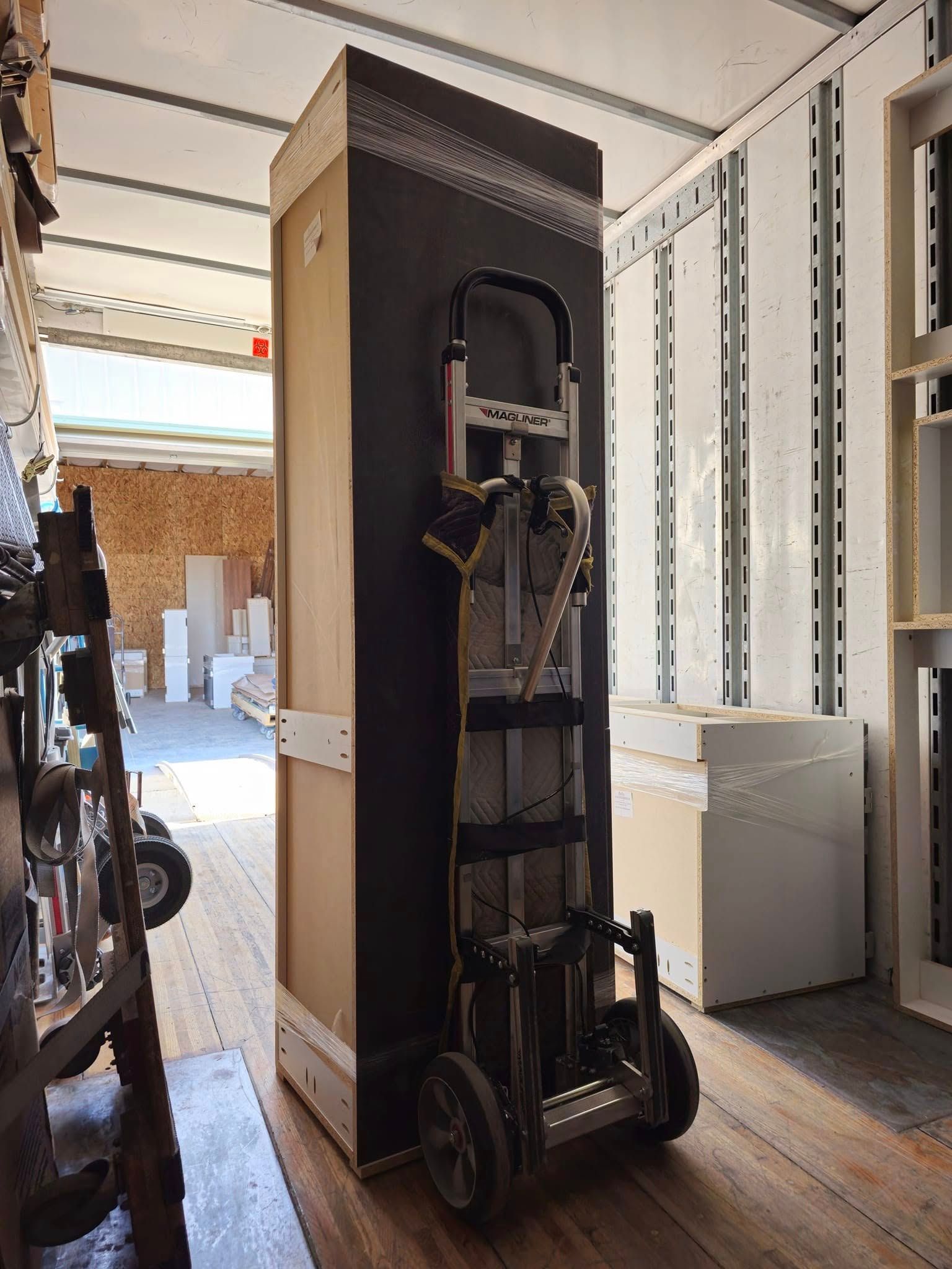 Folded upright wheelchair secured with straps on a dolly in a storage room.