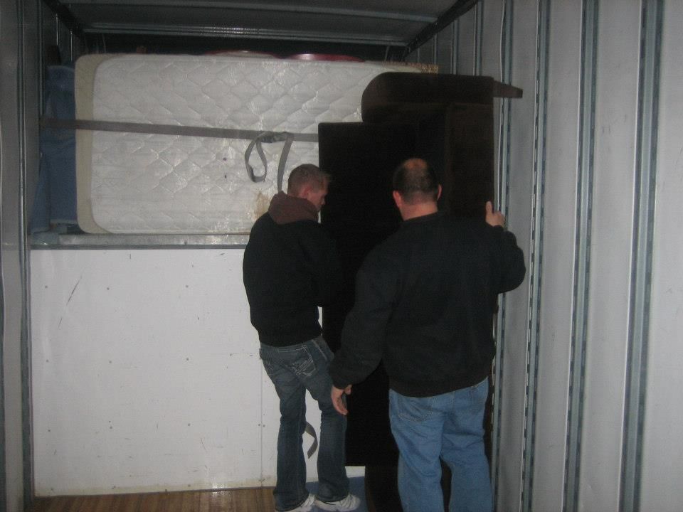 Two men standing in a truck trailer inspecting a large black cabinet or machine.