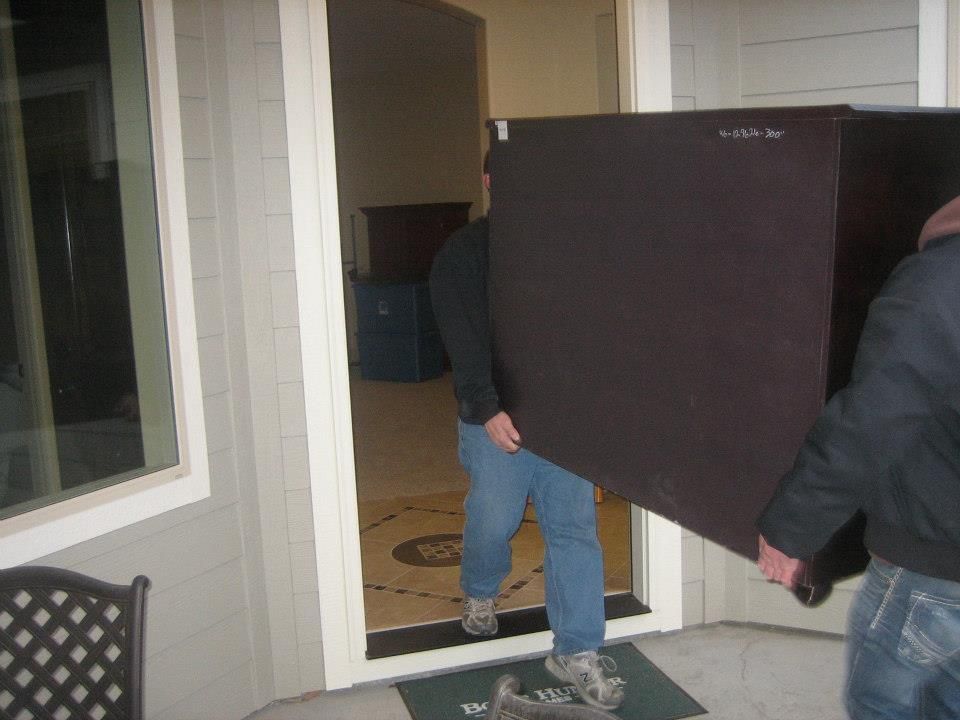 Two people carrying a large black panel through a front doorway onto a porch