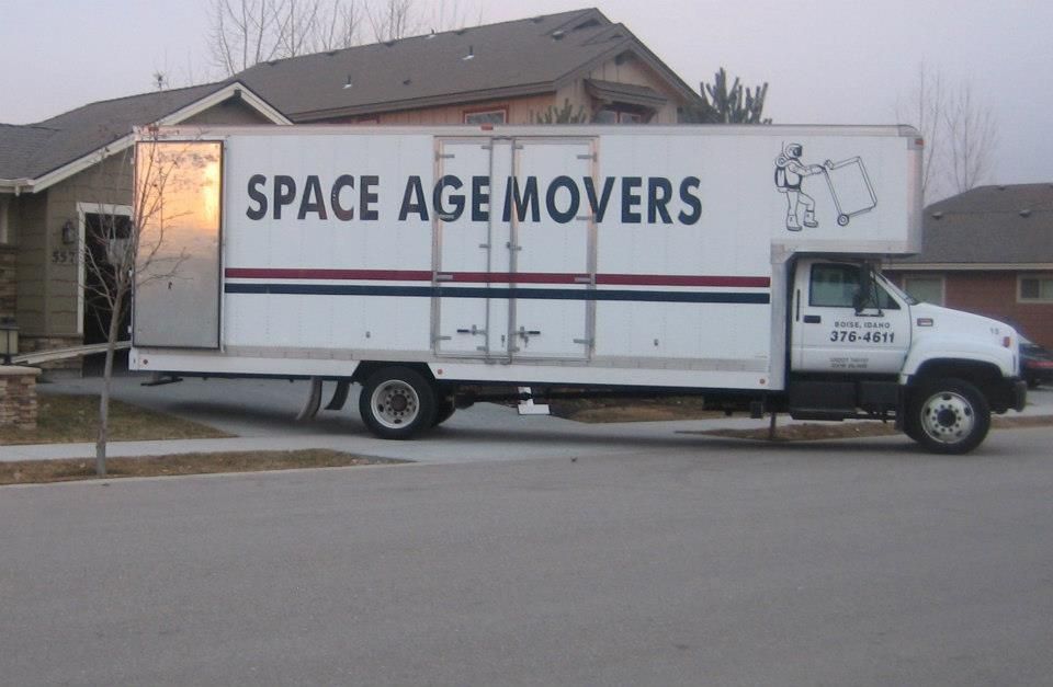 White Space Age Movers truck parked on a residential street with a house in the background
