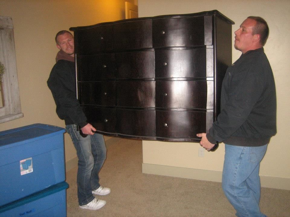 Two men carrying a large black dresser through a room