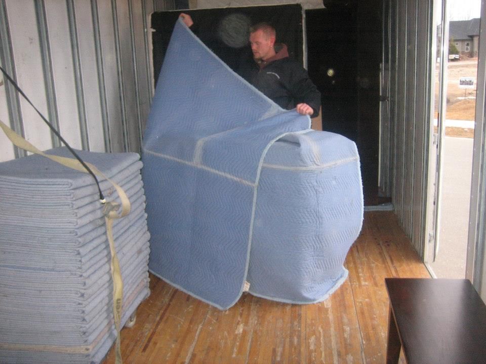 Person moving a large blue upholstered chair through a narrow hallway in a storage area