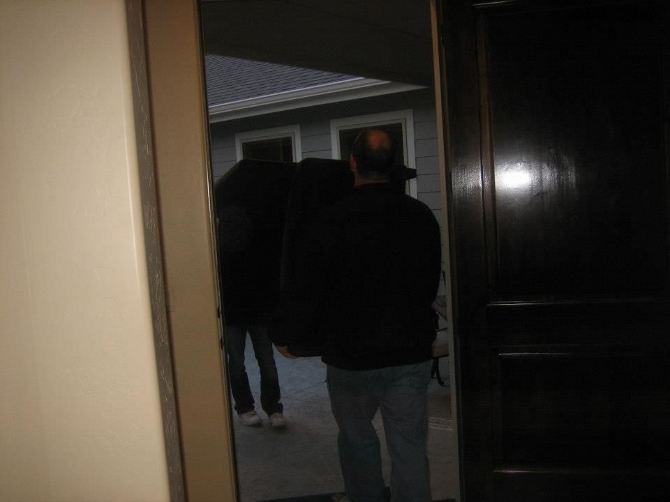 Two people walking toward a house entrance at dusk, seen from inside a doorway.