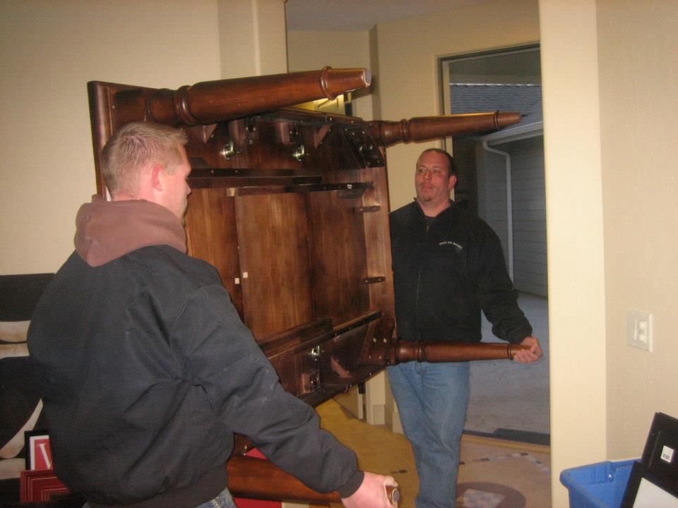 Two men carrying a large wooden cabinet through a doorway in a home interior