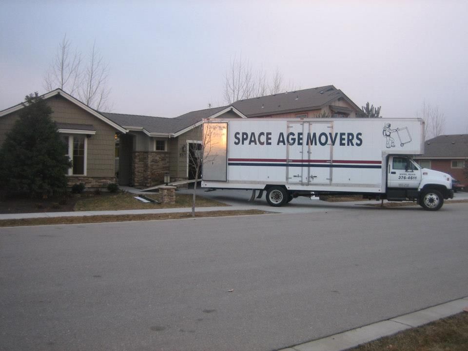 White moving truck labeled “SPACE AGE MOVERS” parked in front of a house at dusk