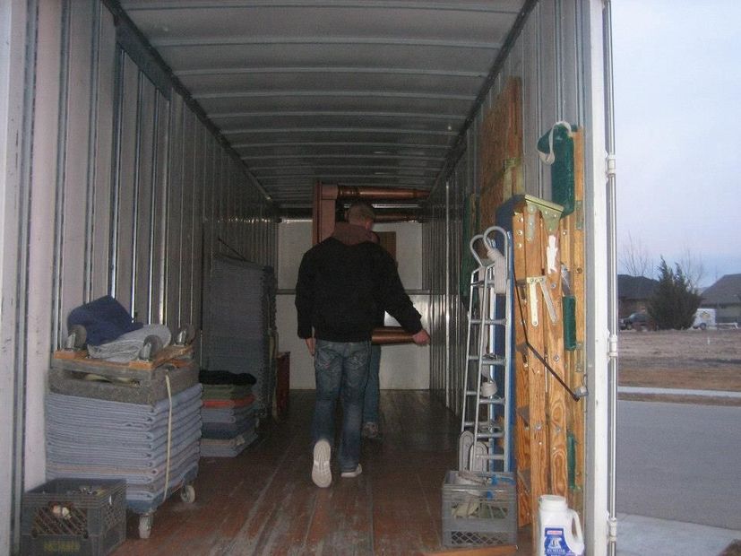 Person walking through a shipping container aisle with stacked boxes and supplies on both sides