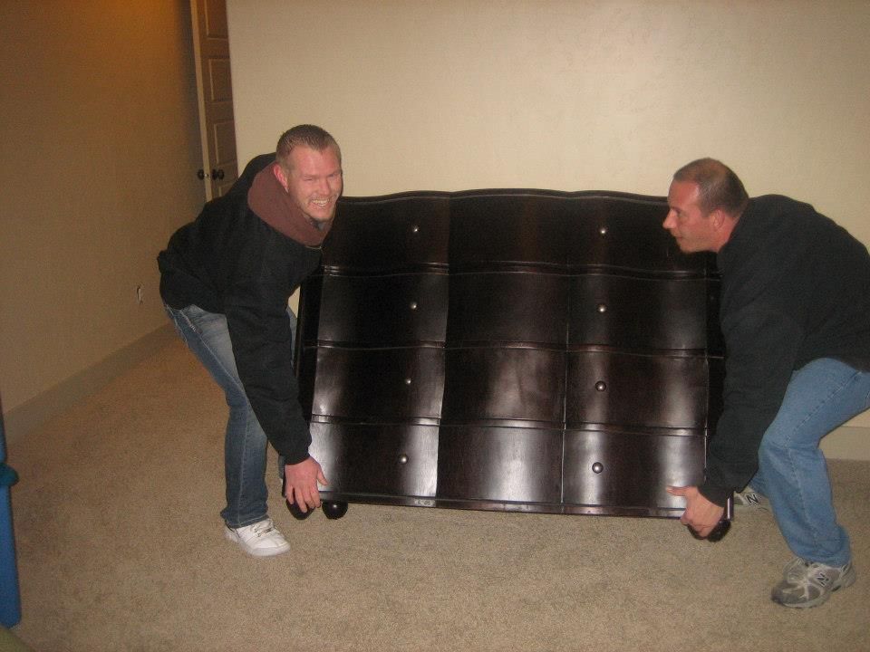 Two men carrying a large black couch indoors, crouching on either side.