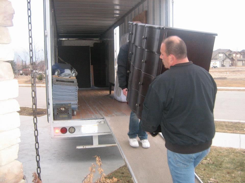 Workers loading a large black cabinet into a truck at a loading dock