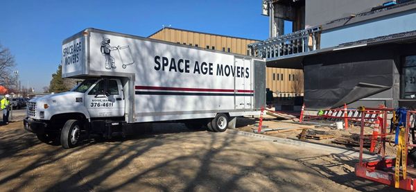 Space Age Movers truck parked by a building under construction with orange cones and caution tape