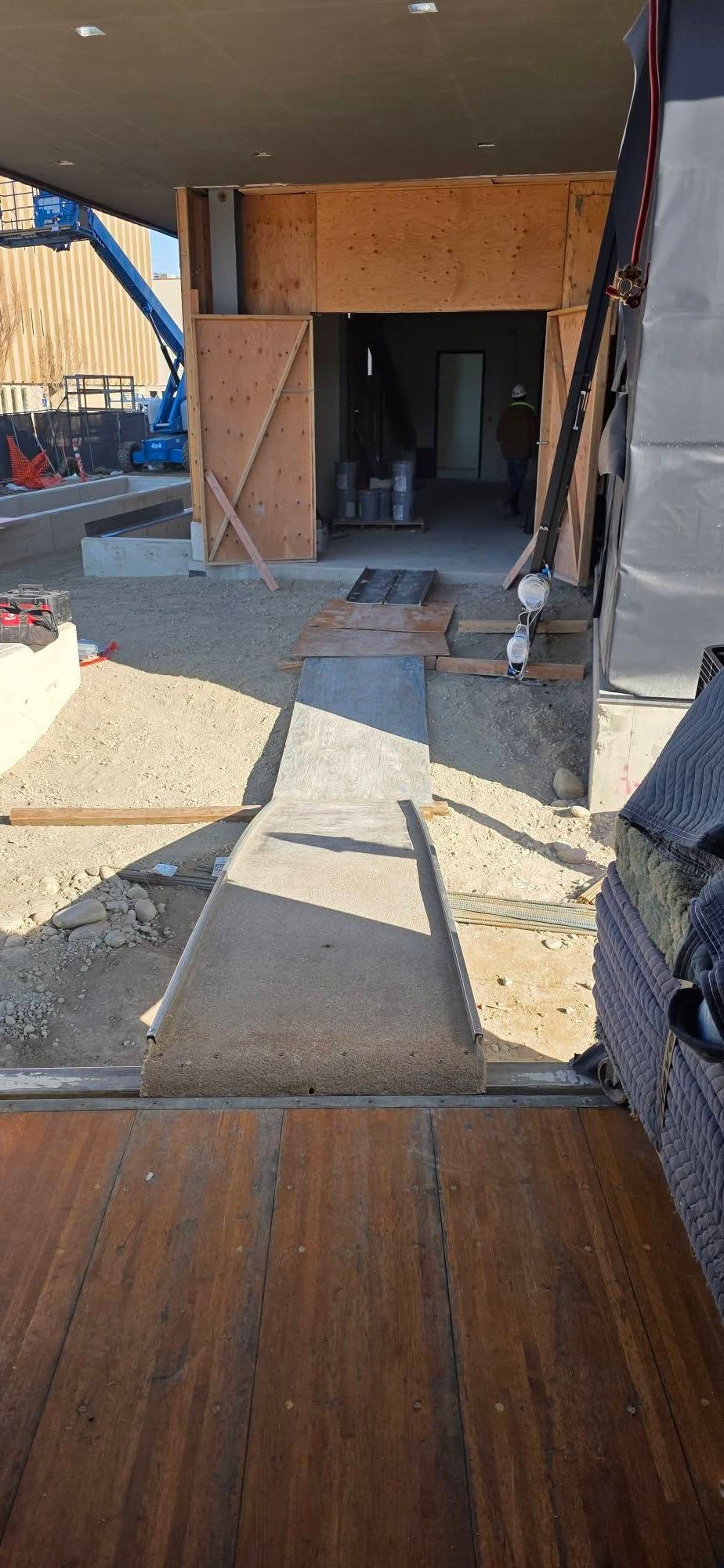 Wooden ramp leading to a dark doorway at a construction site, with temporary barriers and dirt ground.