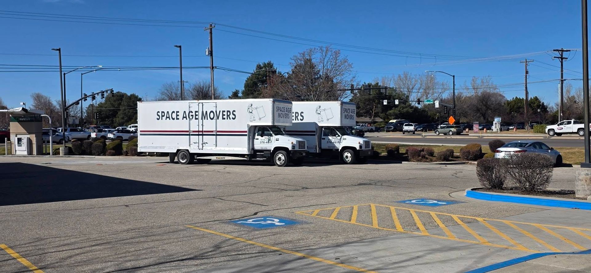 White U-Haul box truck parked in a lot under a clear blue sky with a black pickup nearby.