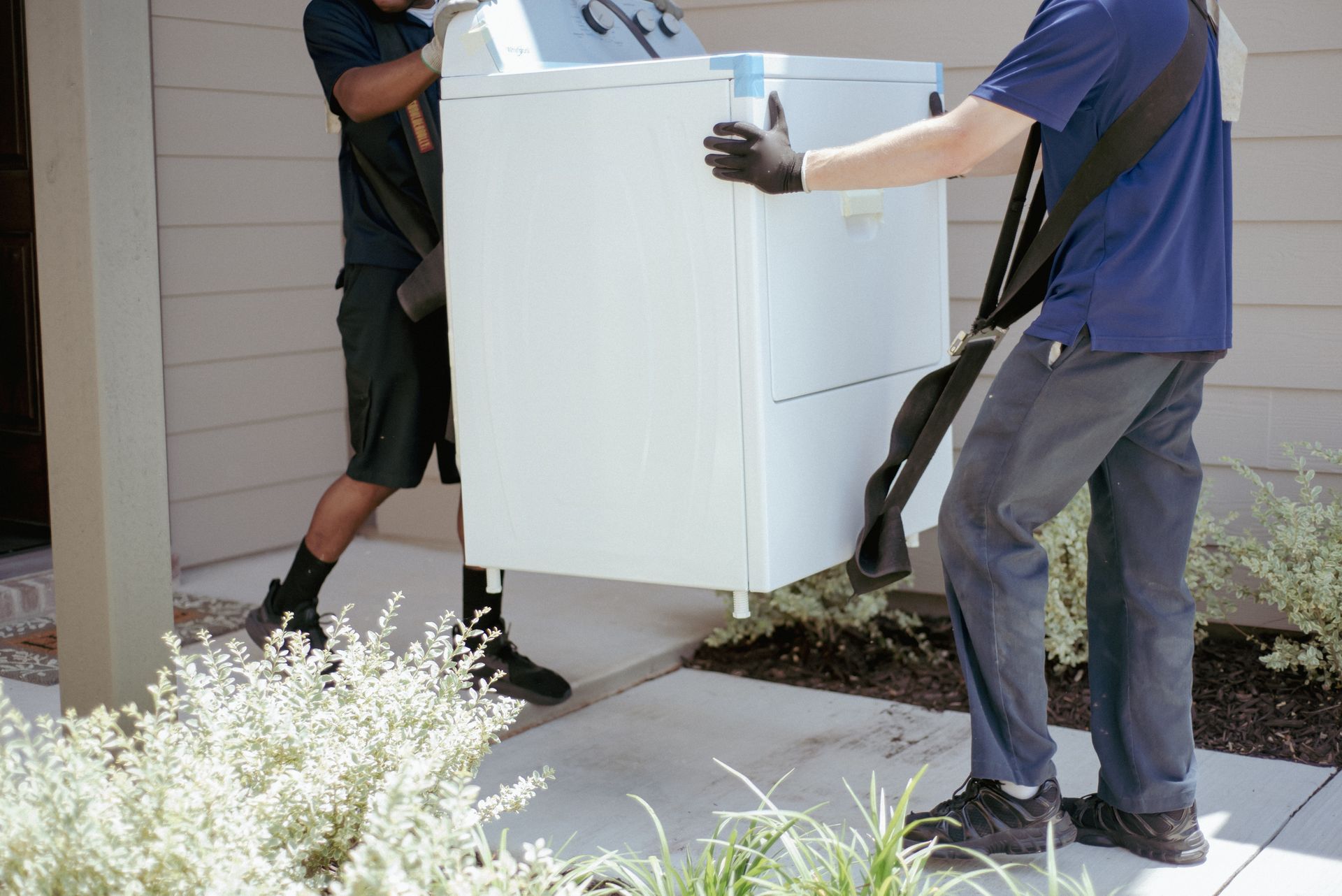 Two workers carrying a large white appliance up a front walkway