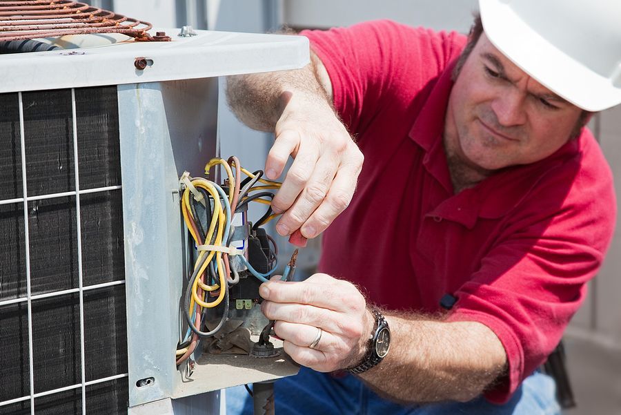 A man wearing a hard hat is working on an air conditioner