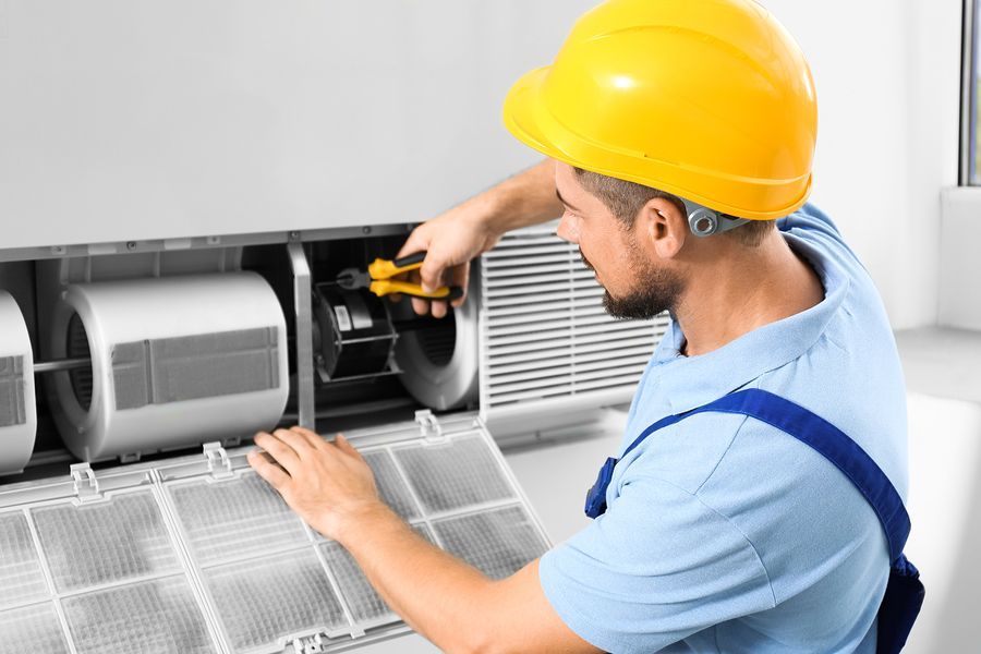 A man wearing a hard hat is working on an air conditioner