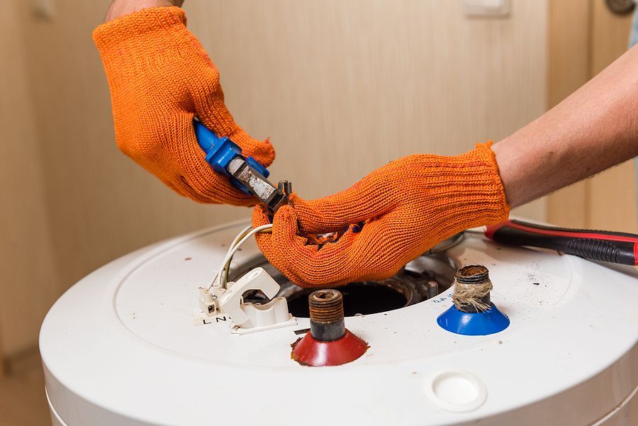 A man wearing orange gloves is fixing a water heater.