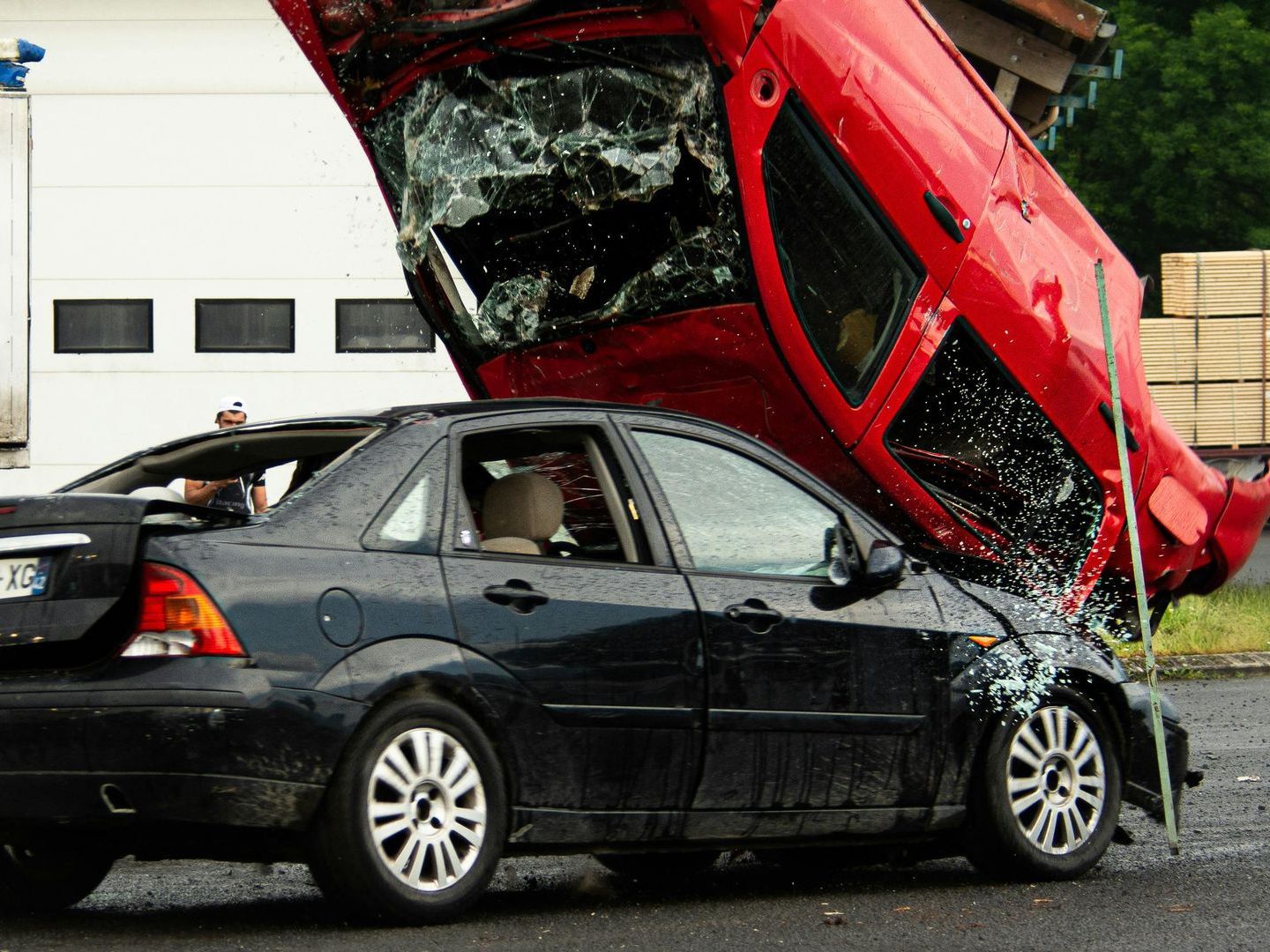 A person is writing on a clipboard in front of a car with a broken windshield.