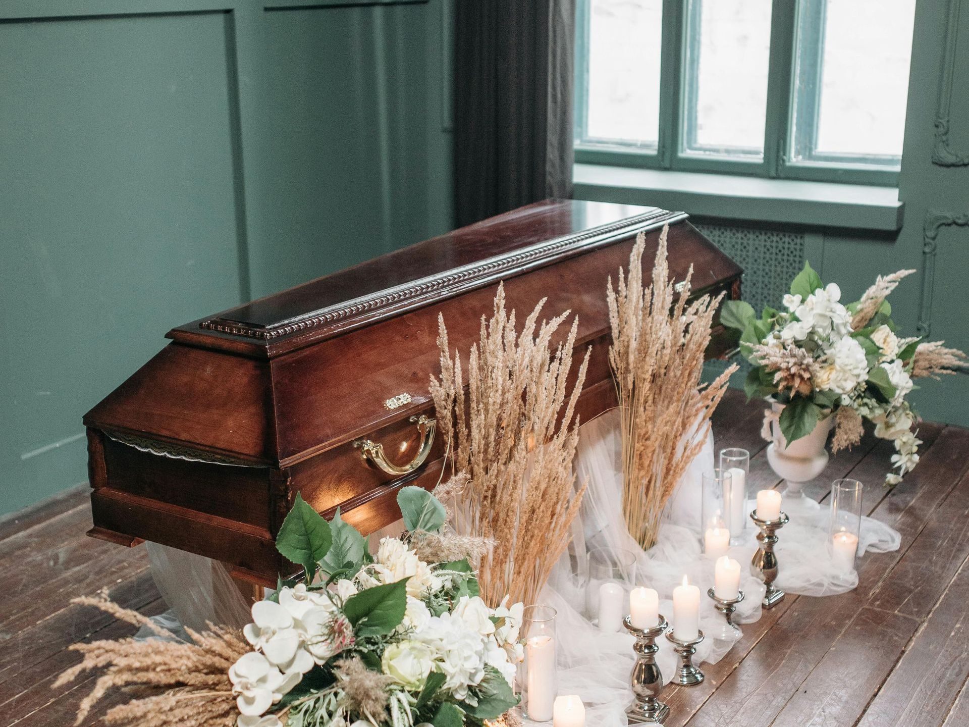 A coffin is sitting on a wooden table with candles and flowers.