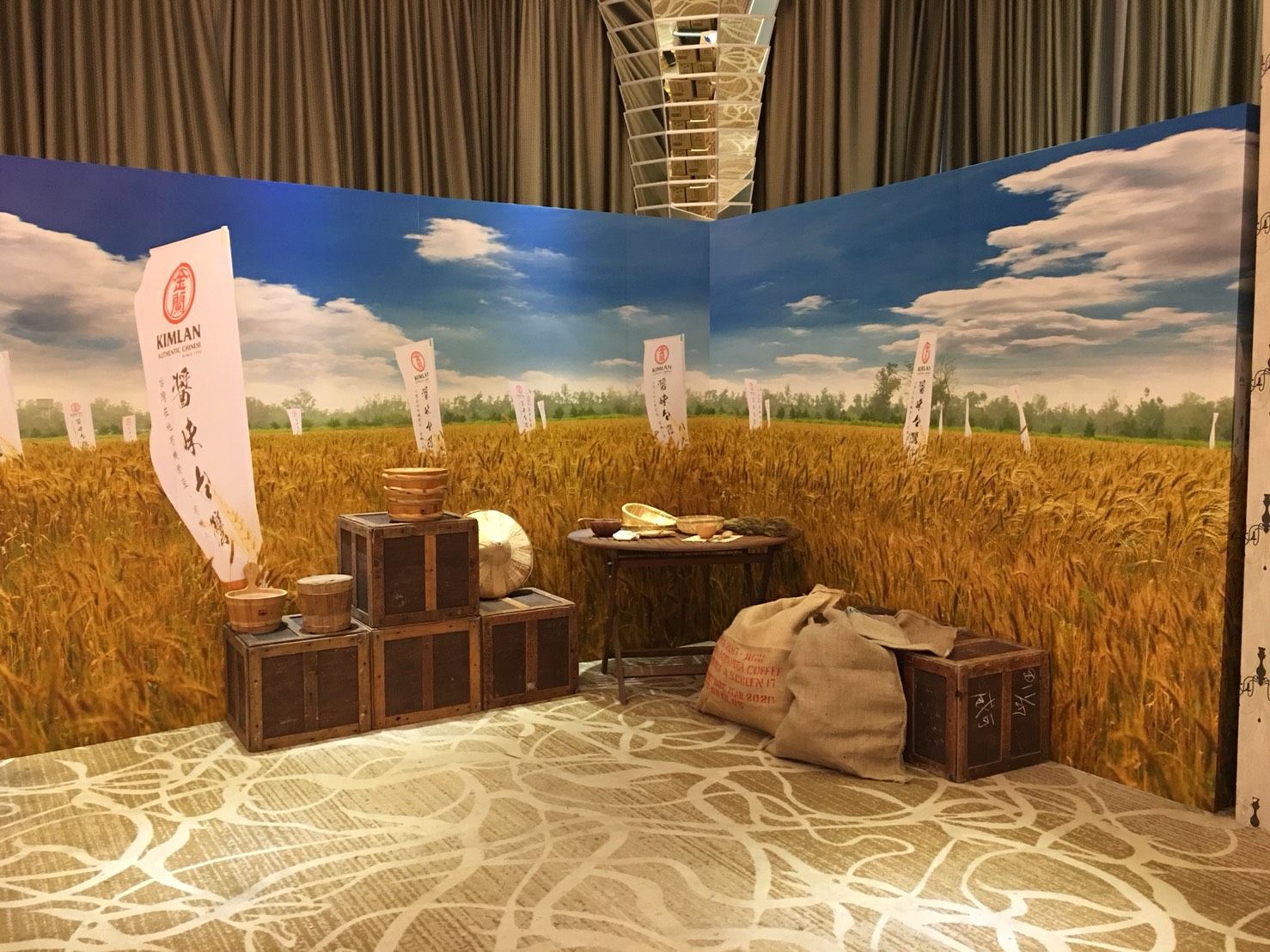 Display booth with wheat field backdrop; wooden crates and bags; table with bowl.