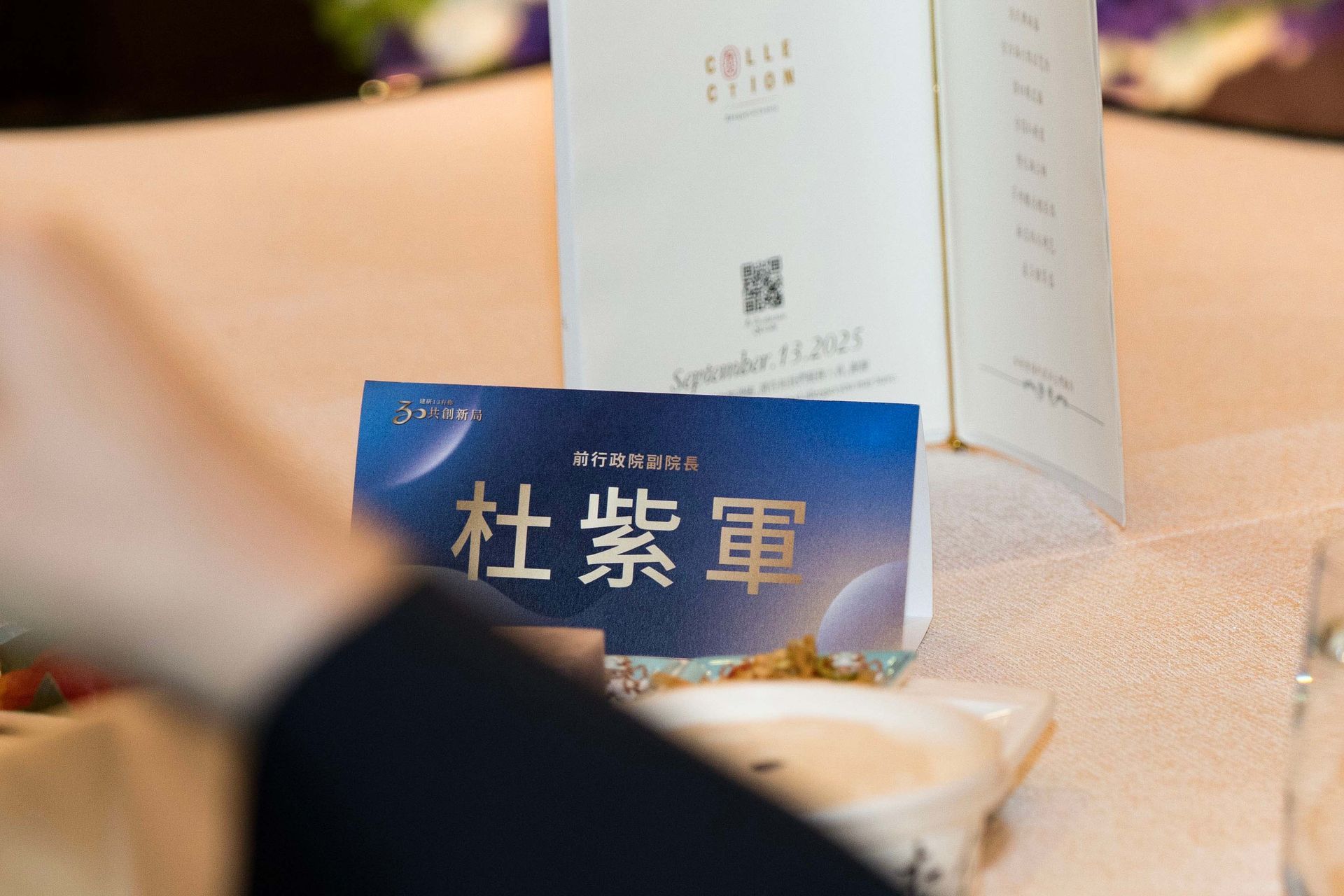 Table setting with a name card in Chinese characters, a menu, and a person's arm.