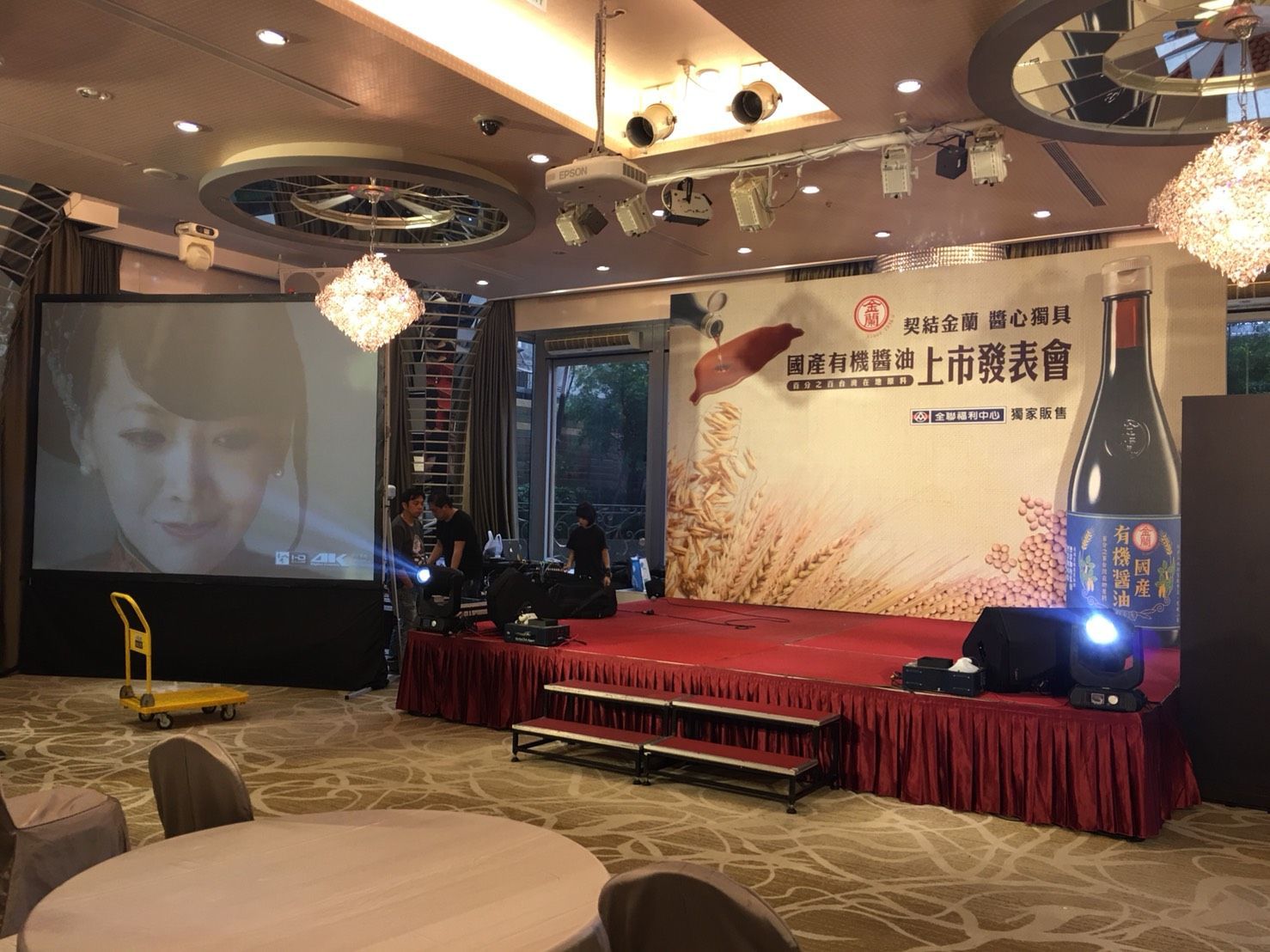 Event stage with a screen showing a woman, a red stage, and a banner.