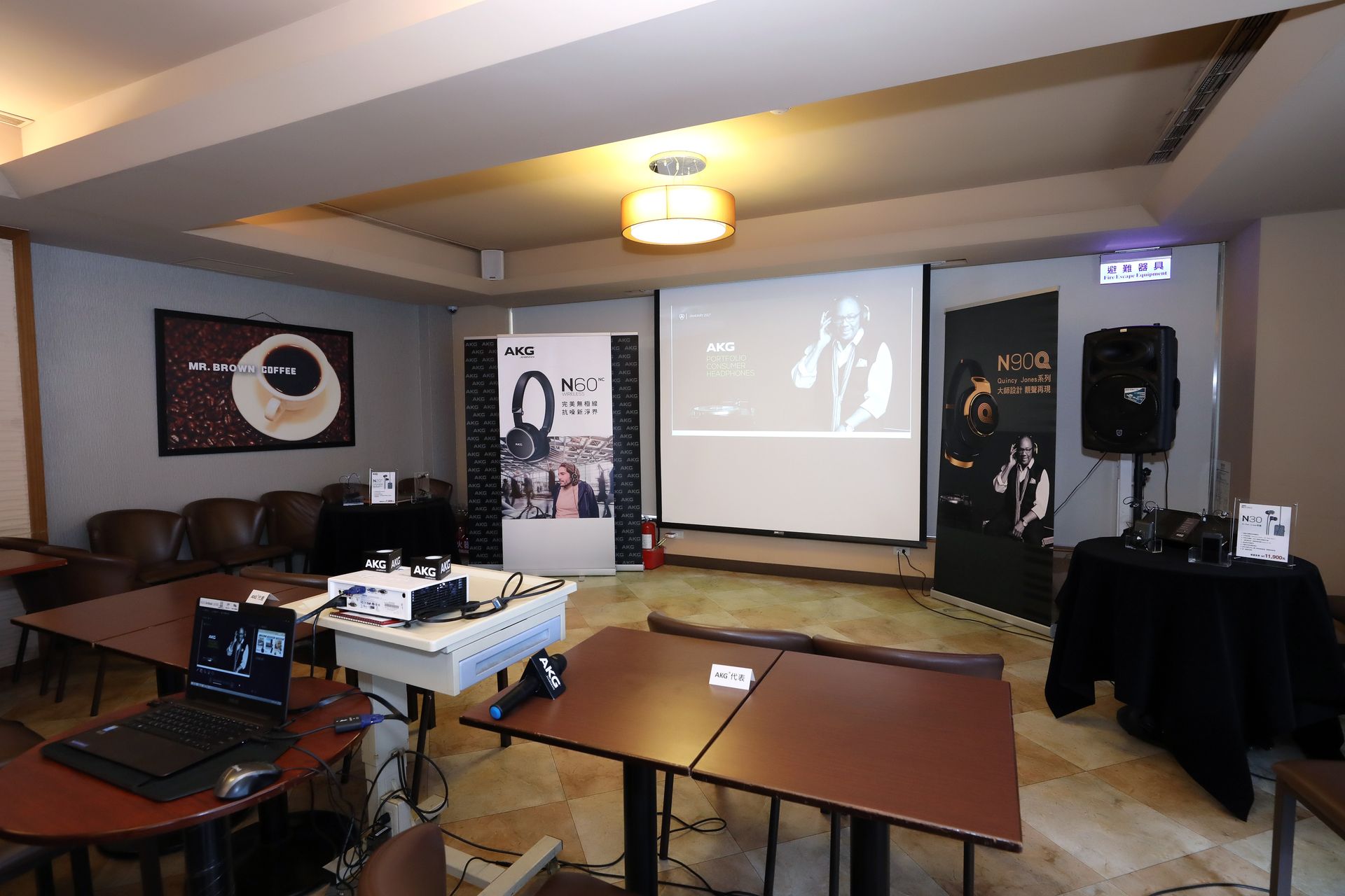 Event space set up with tables, projector screen, sound equipment, and posters; a film is playing.