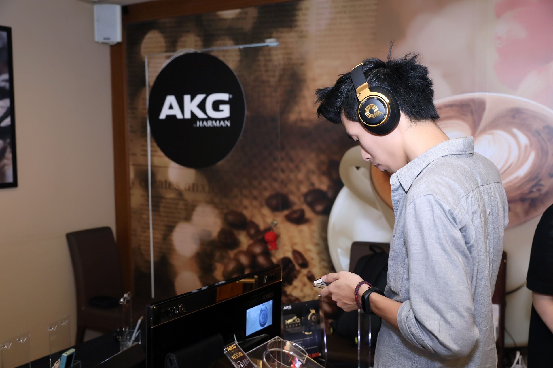 Person wearing headphones, using a device, next to an AKG logo sign.