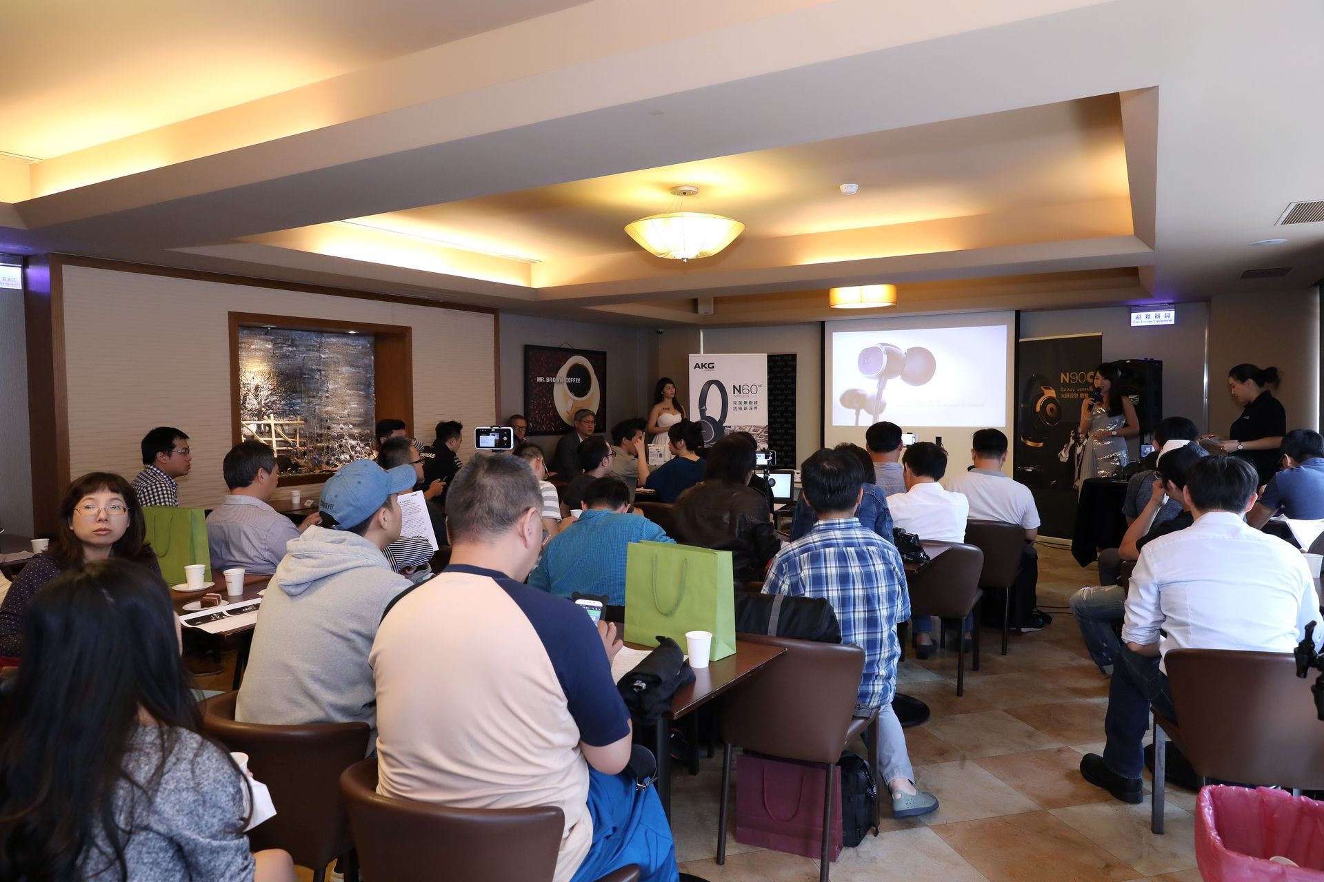 Audience at a conference in a hotel room with a presentation on a screen.