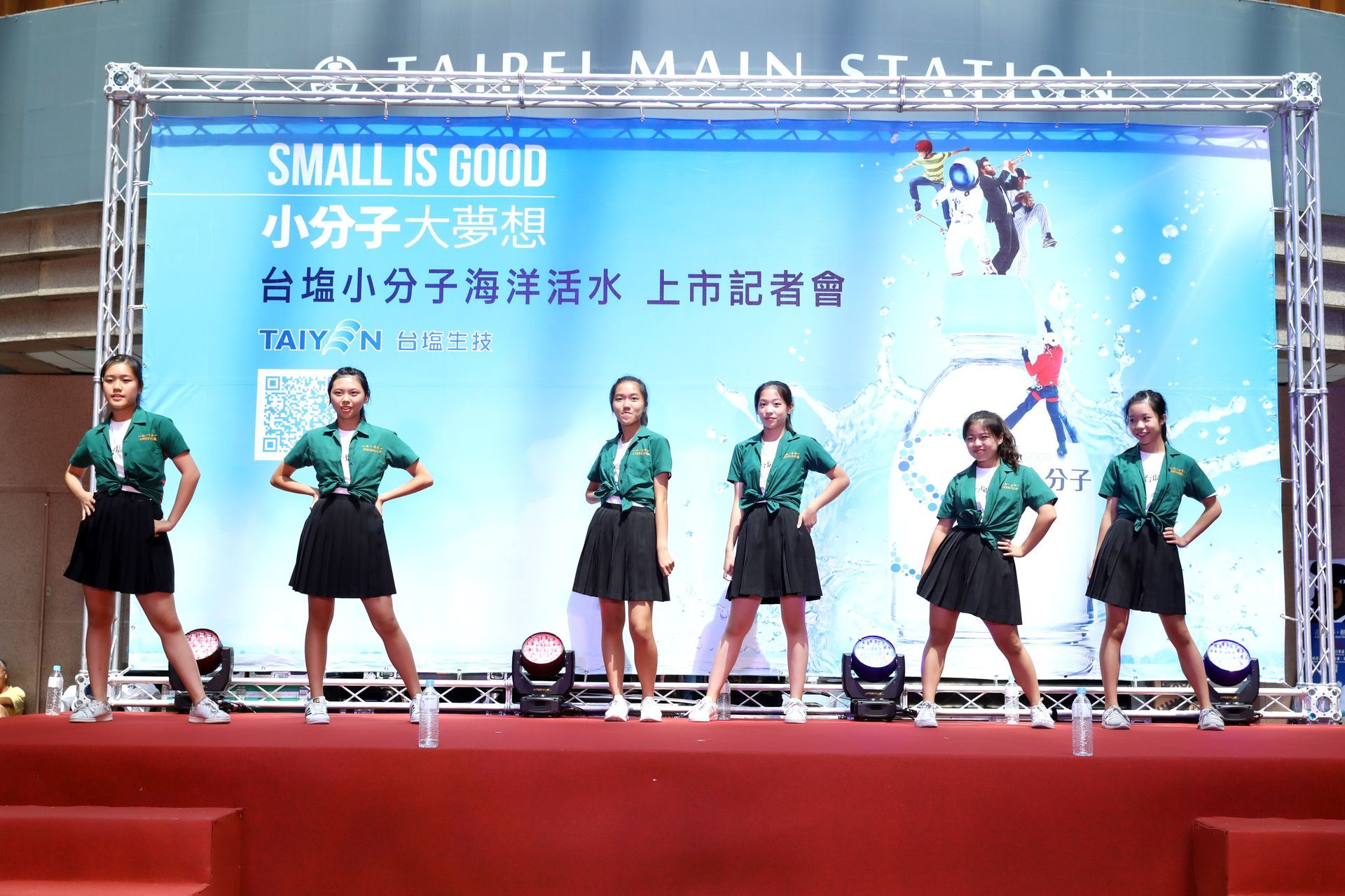 Six young dancers on stage at Taipei Main Station, promoting a product.