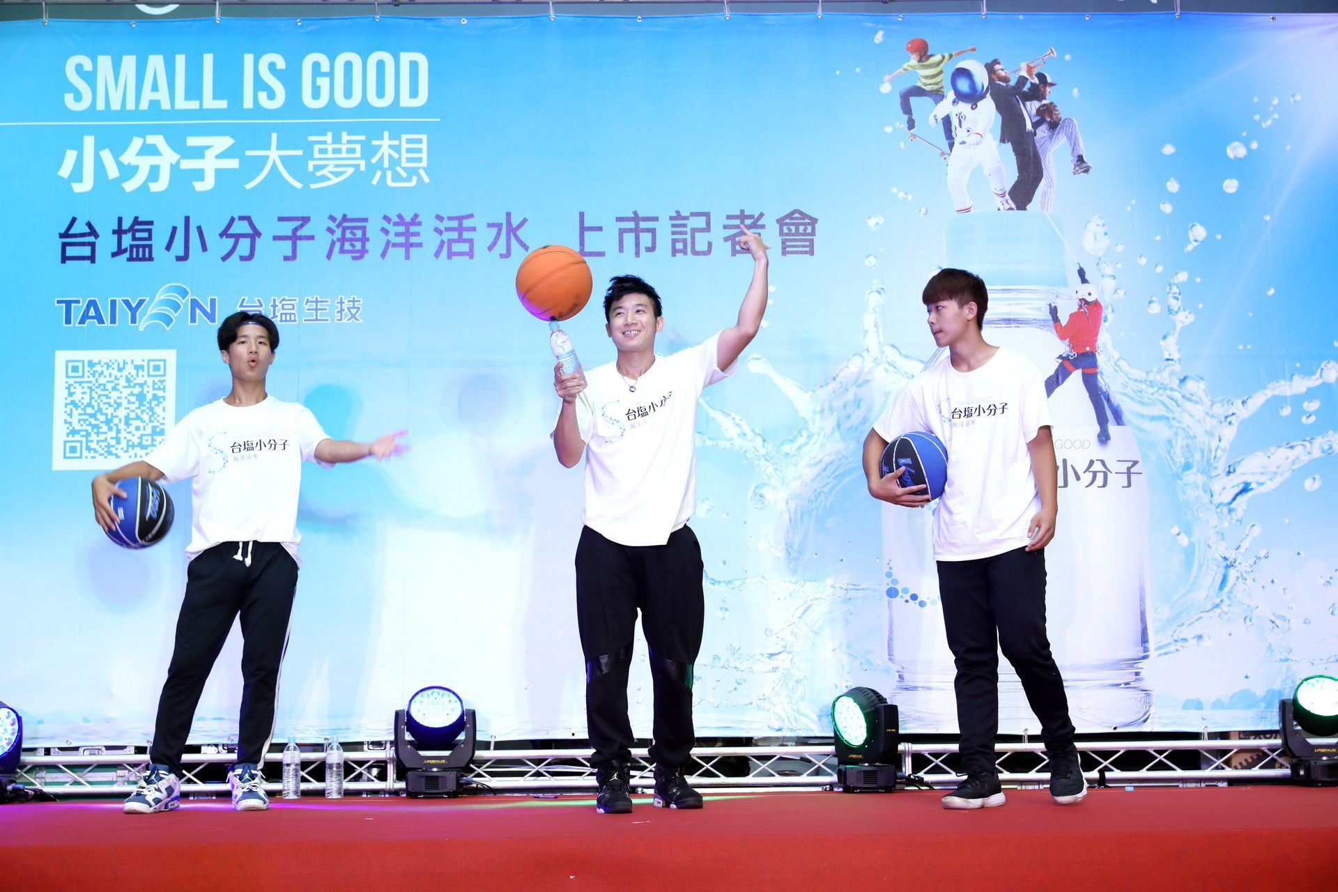 Three men at a product launch; one spins a basketball. Background has product logo and water splash art.