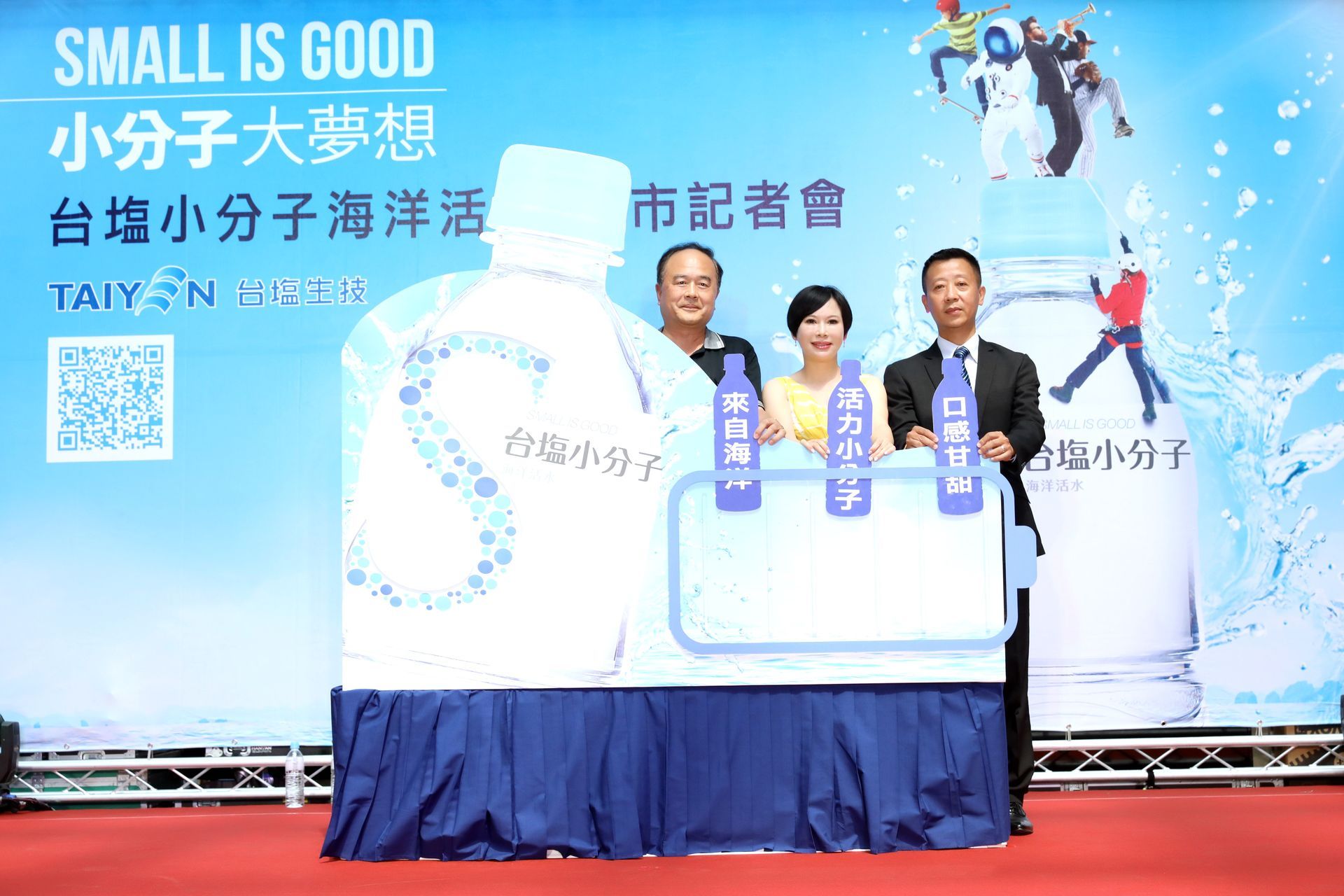 Three people stand at a press conference; backdrop has text and a water bottle graphic.