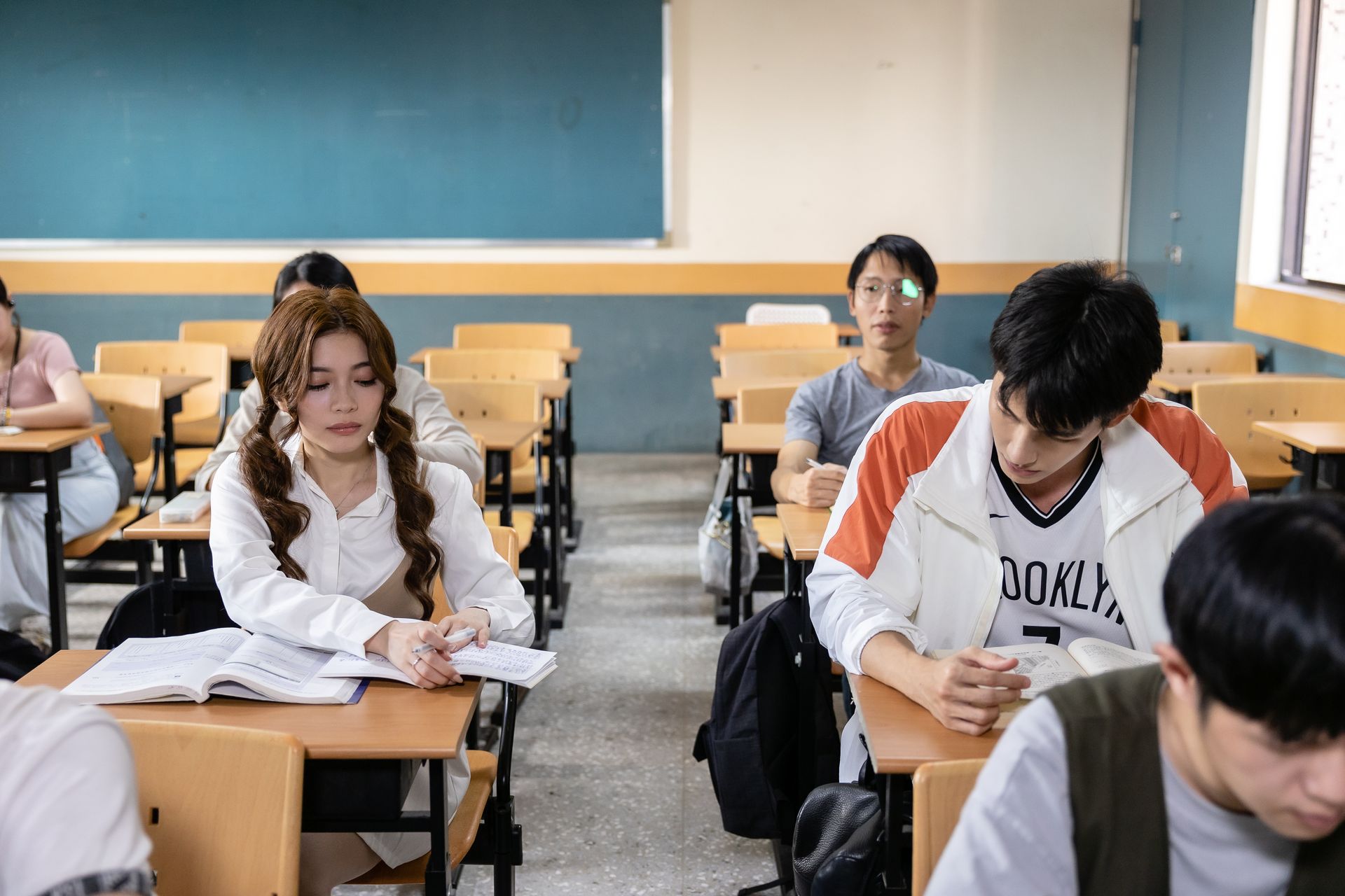 Students in a classroom. A young woman with pigtails takes notes, while other students look forward.