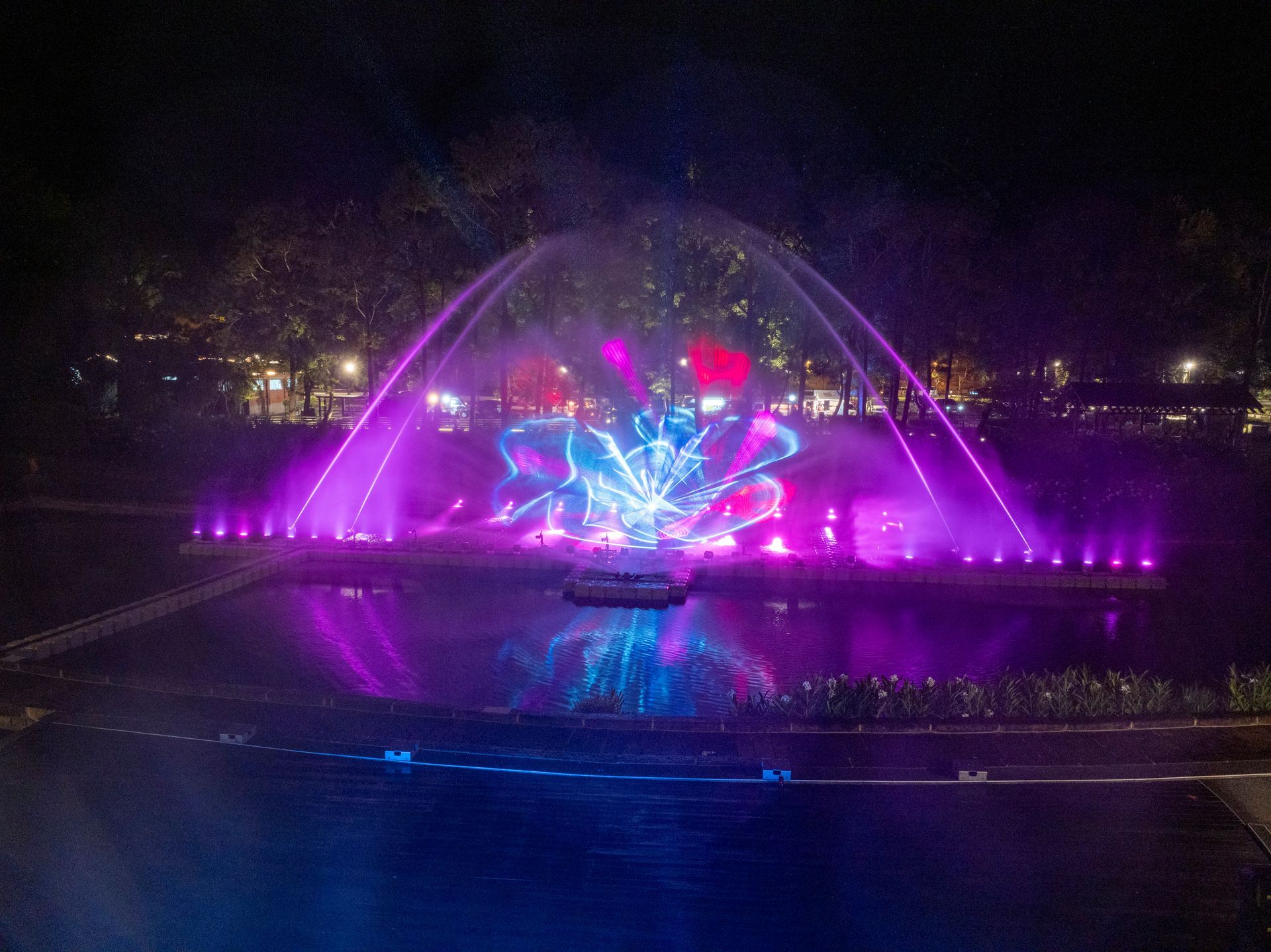 Nighttime water fountain show with bright purple and blue lights.