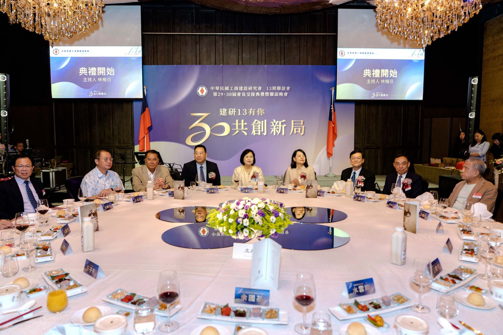 People seated at a round table, toasting drinks. Banner reads 