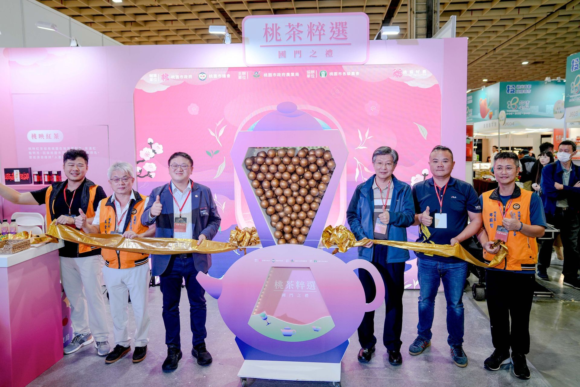 Group of people cutting a ribbon at a pink tea exhibition booth.