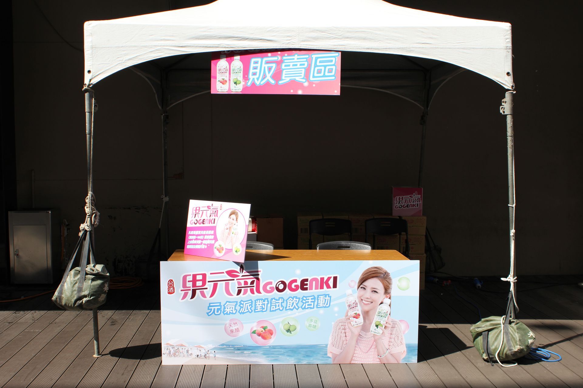 A product display table under a white tent; banner displays product info and a woman holding a product.