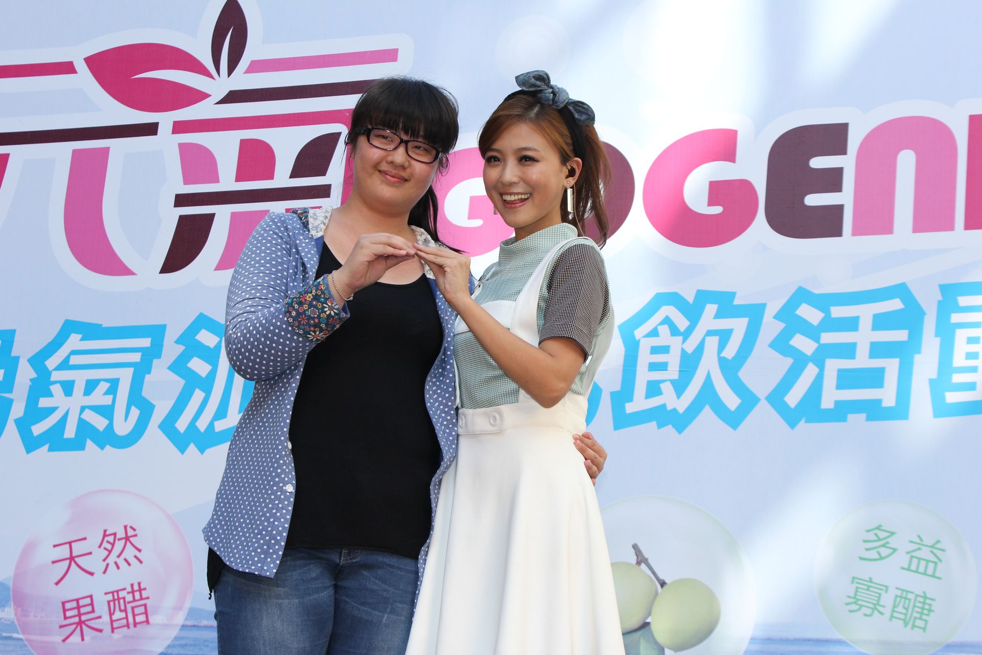 Woman with glasses and another woman posing, both forming heart shapes with their hands.