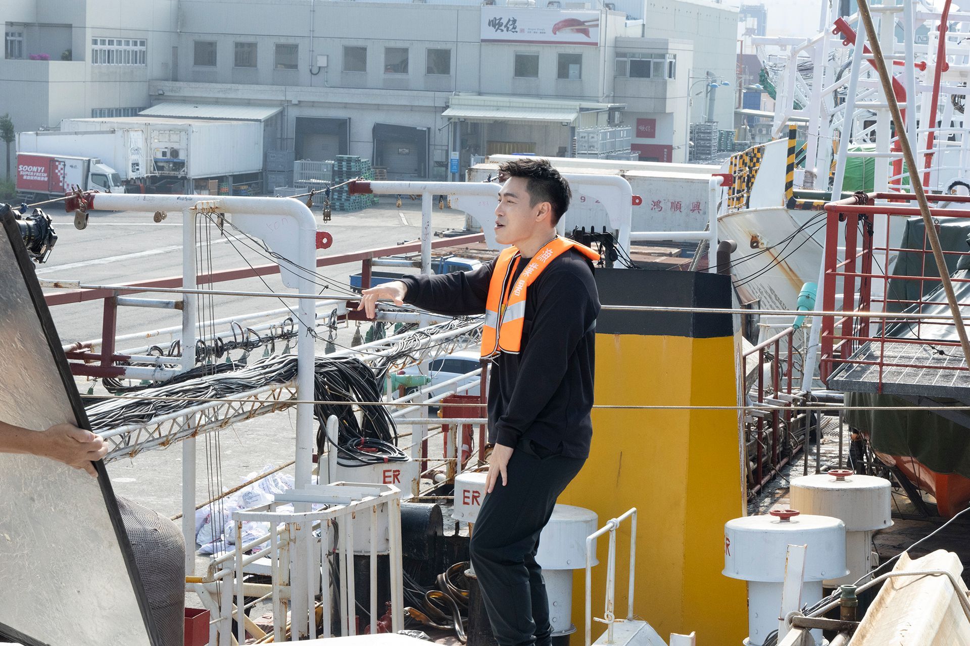 Man wearing life vest points on a boat, bright sunlight.