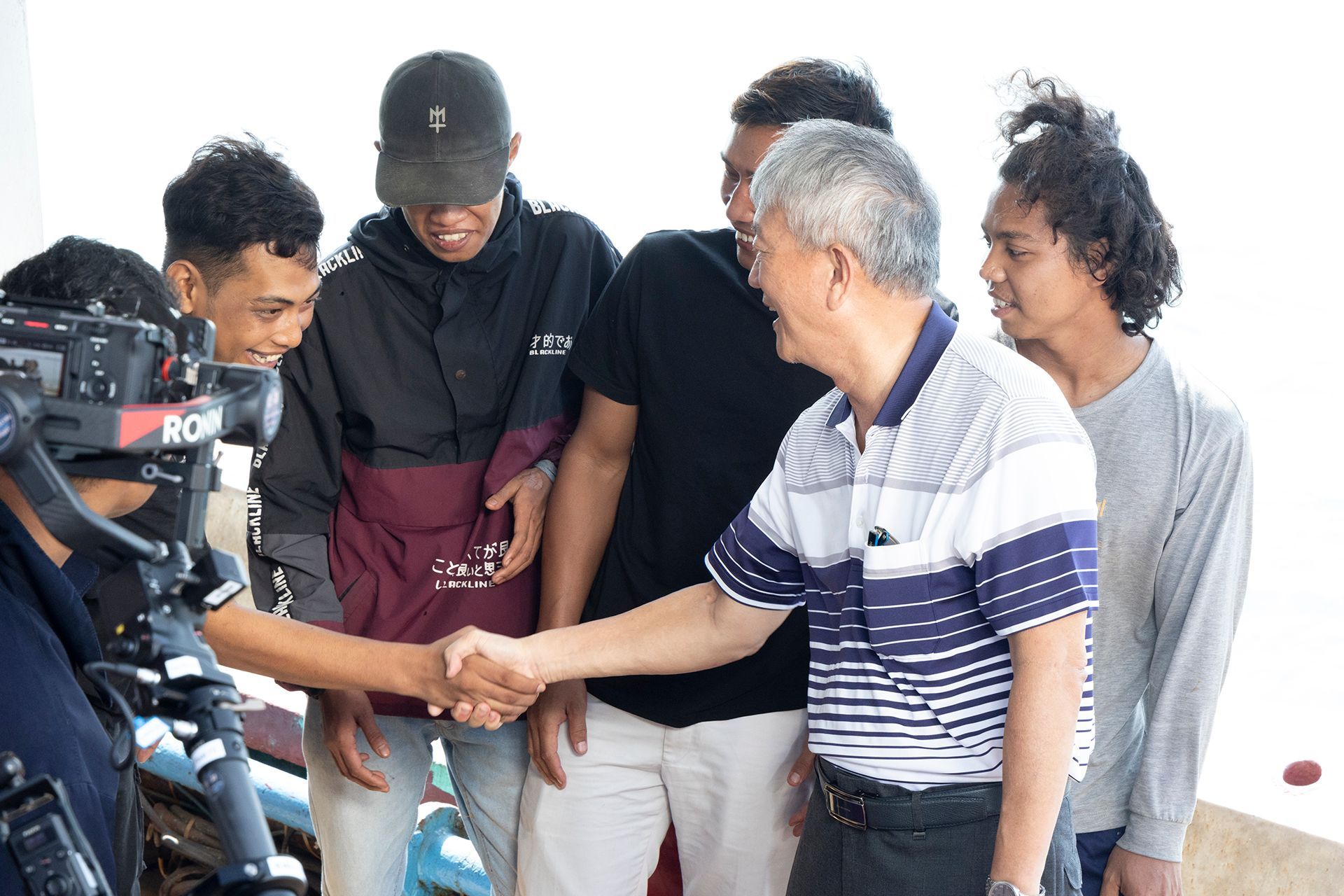 Man shakes hands with another man, surrounded by a group of people.