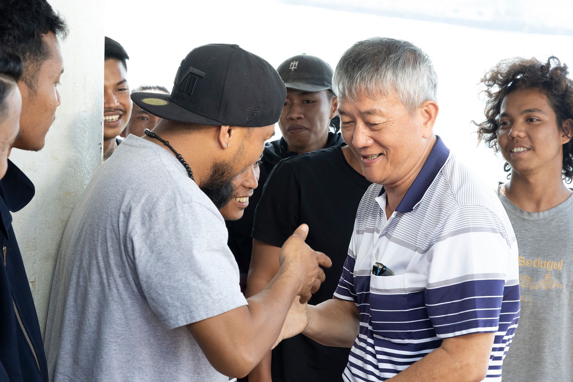 Man in baseball cap shaking hands with another man, surrounded by a group. Outdoors.