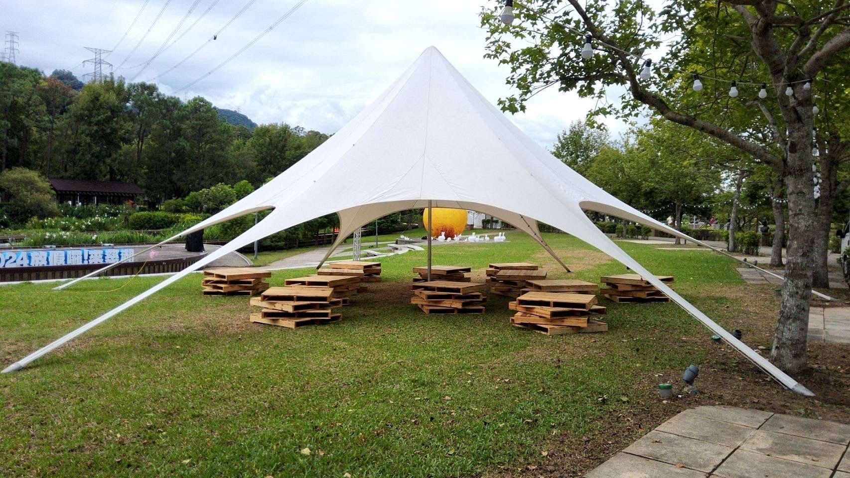 White tent over wooden pallets on a grassy area near a body of water and trees.