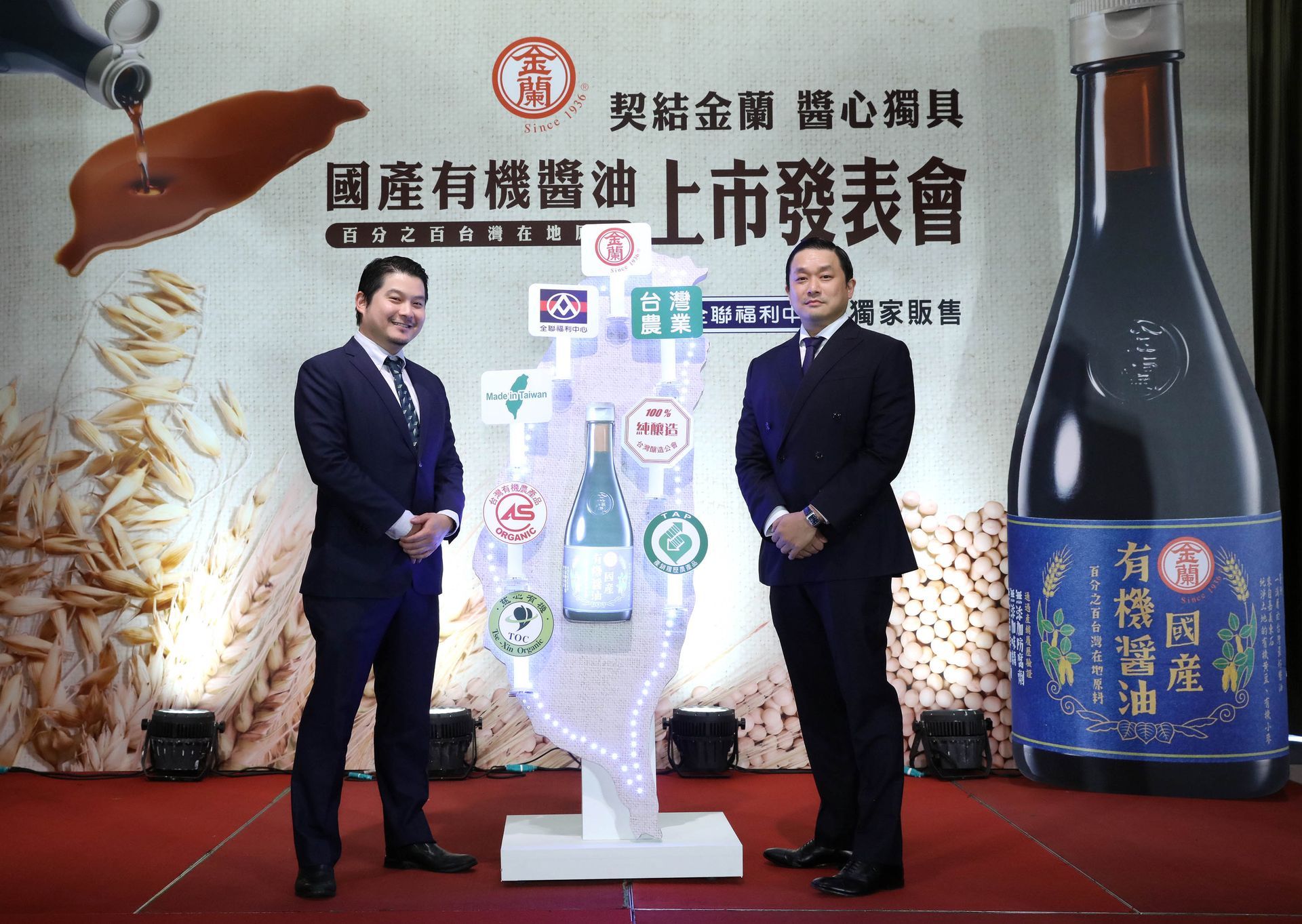 Two men in suits at a podium, presentation for organic soy sauce launch.