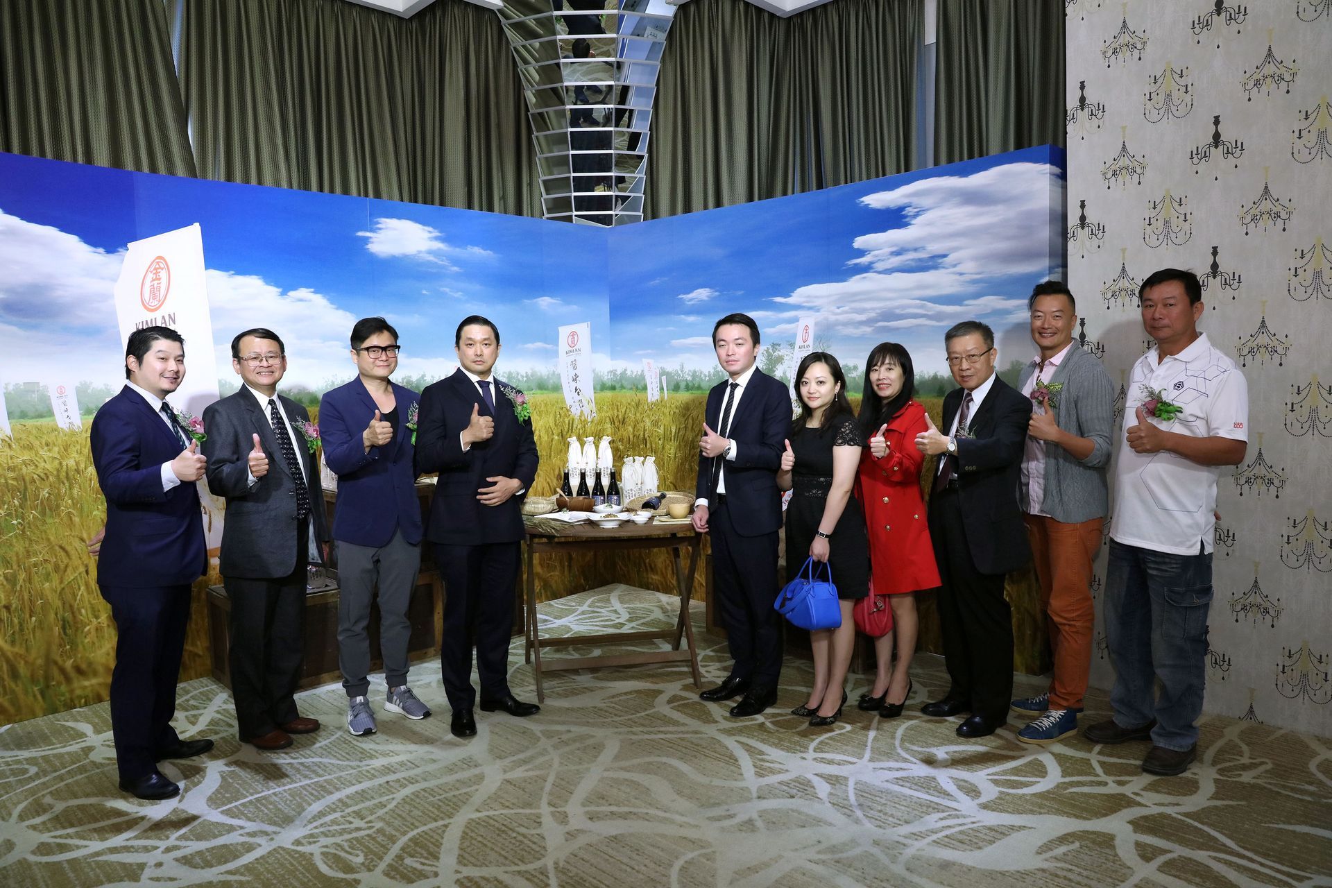 Group of people posing with products in front of a backdrop with a field and blue sky.