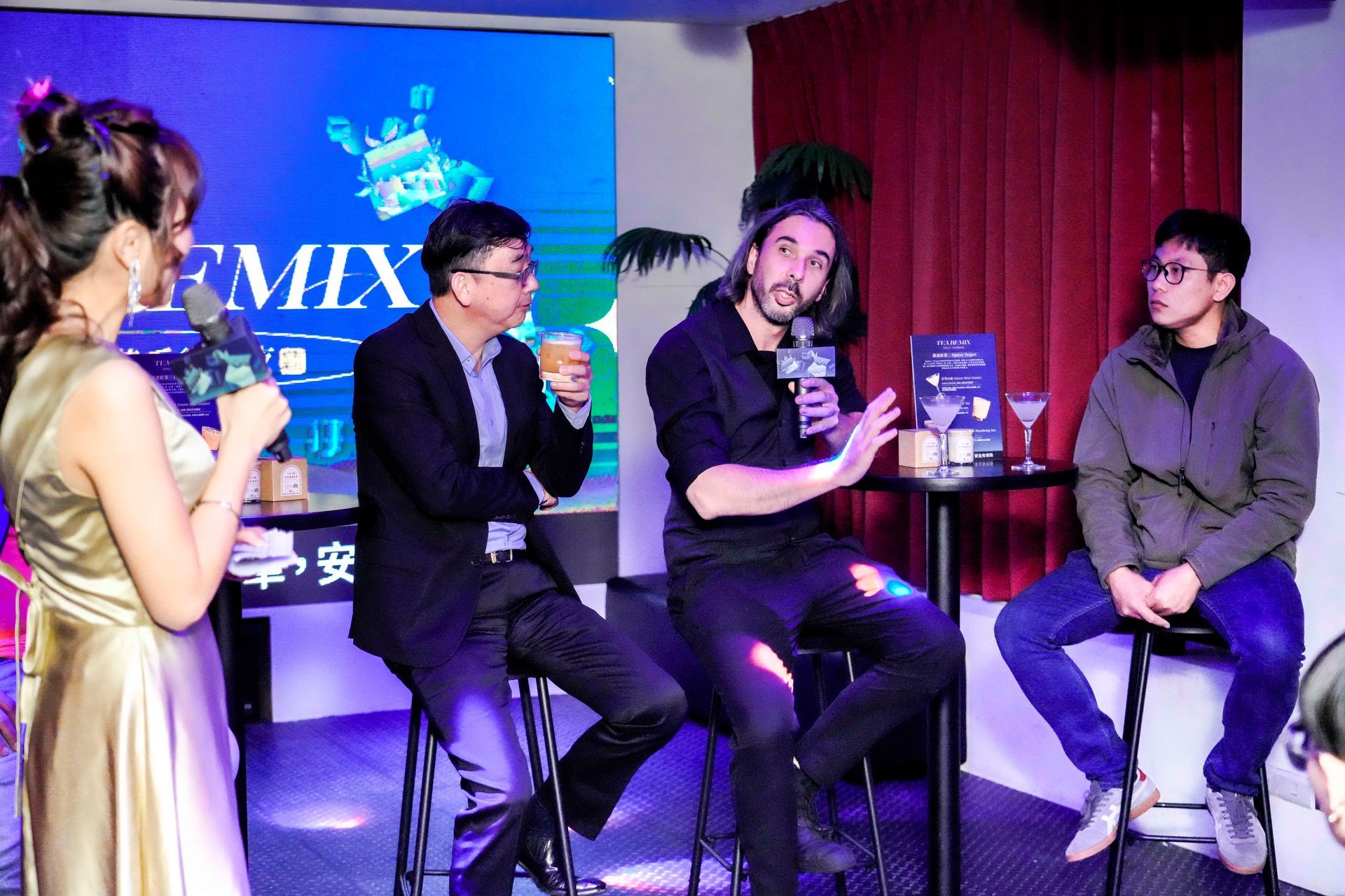 Panel discussion at event with four people seated, microphones, blue backdrop, bar setting.