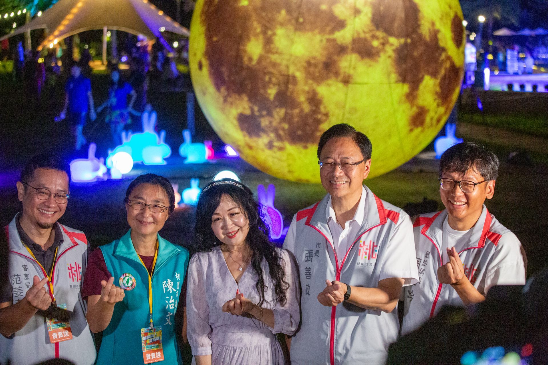 Five people smiling in front of a giant illuminated moon. They are at an outdoor event at night.