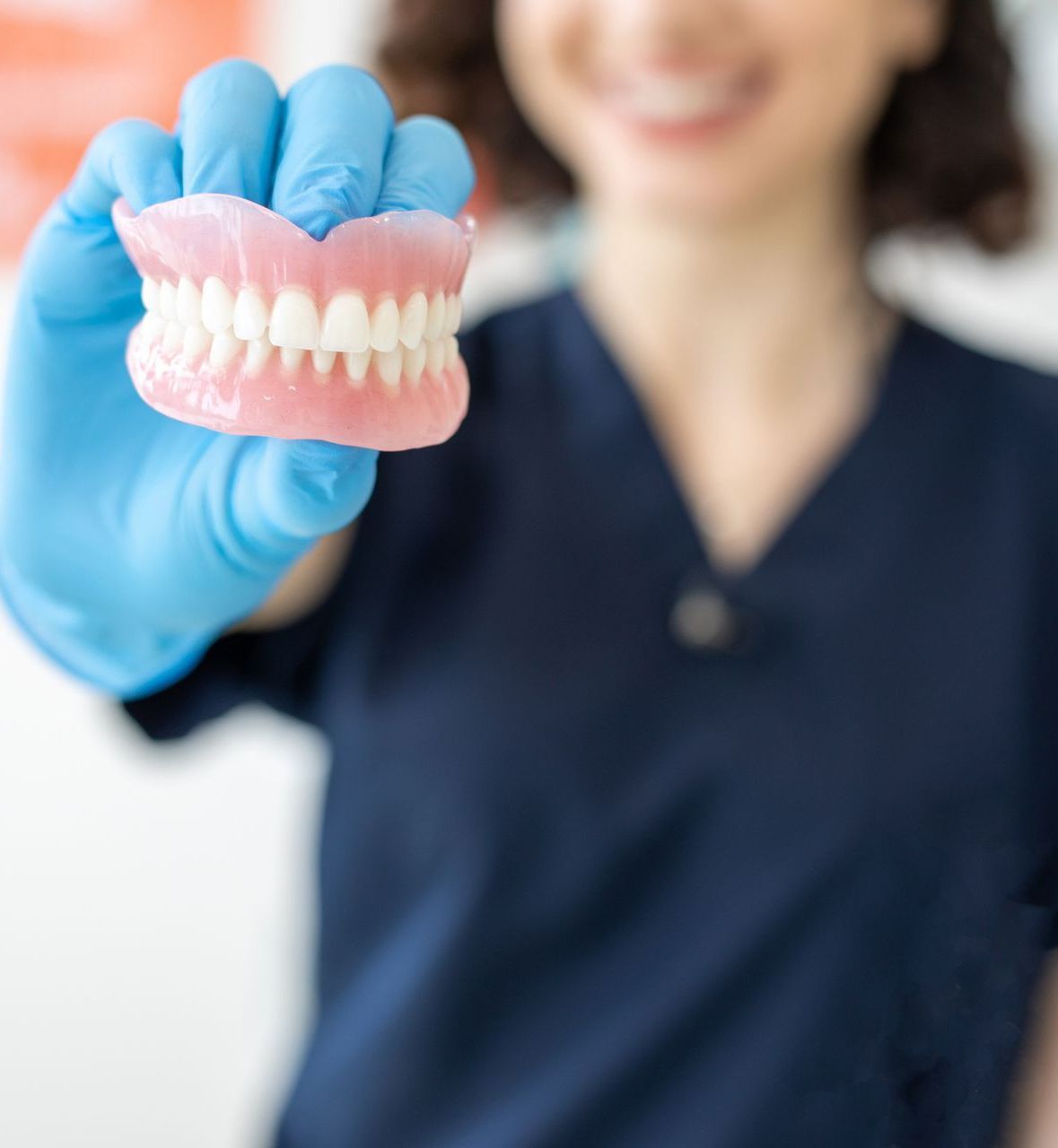 Gloved hand holding a pink dental dentures model in a clinical setting