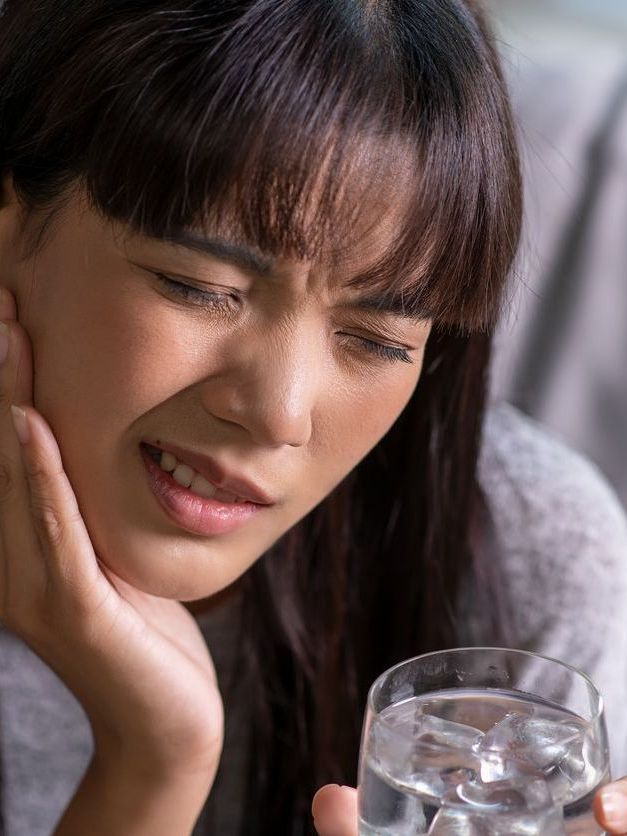 A woman is holding her face in pain while holding a glass of water.