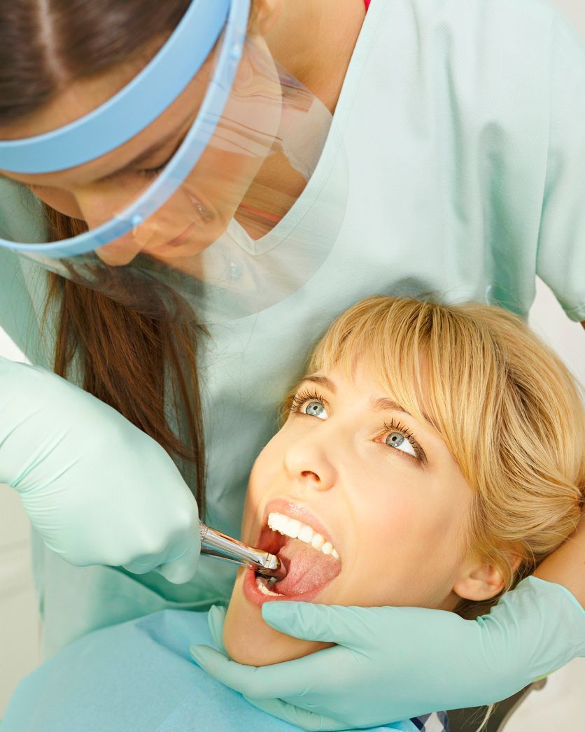 Dentist examining a patient’s open mouth with gloved hands and dental tools.