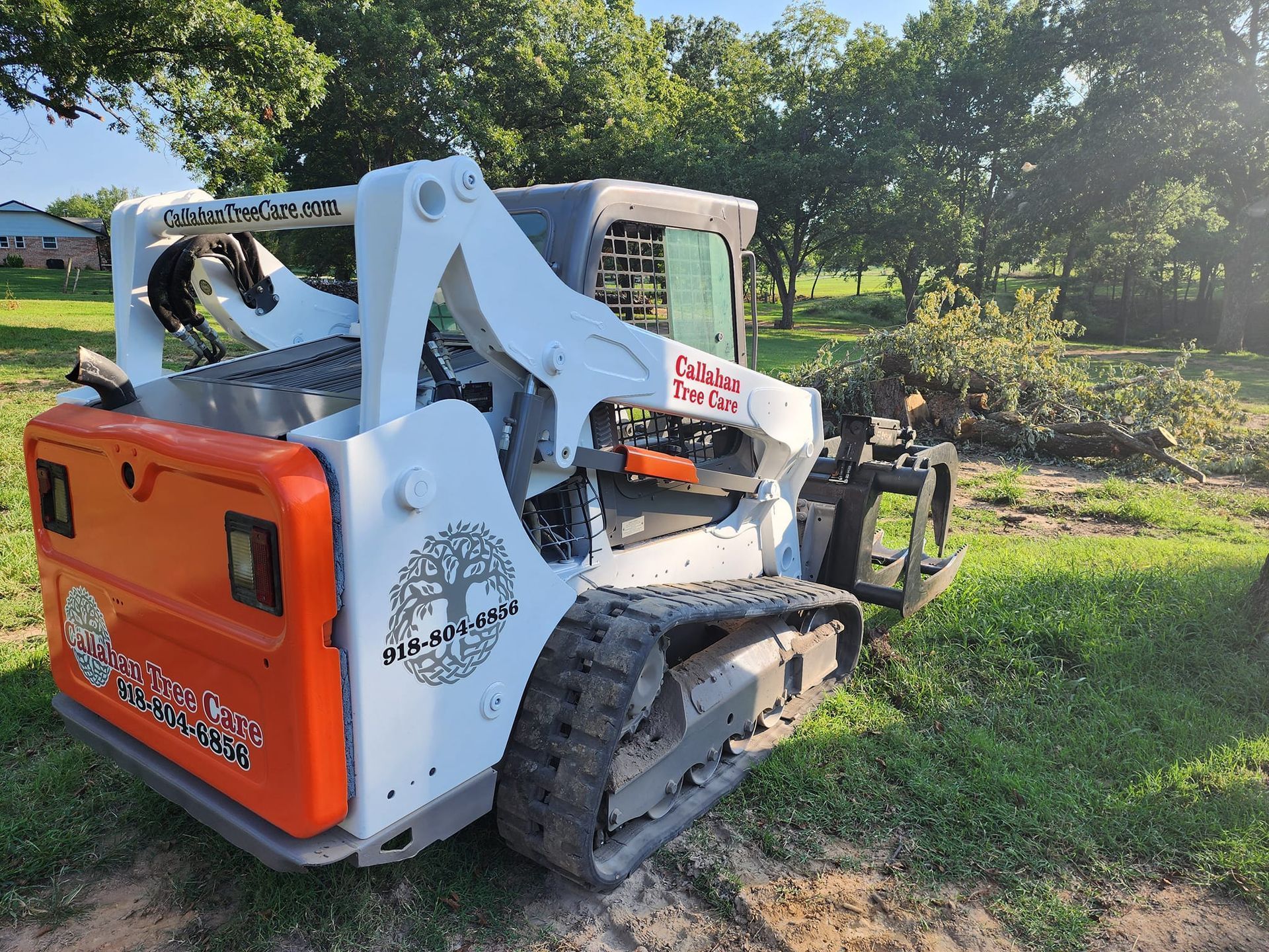 Orange and white Bobcat skid steer parked on grass in a sunny wooded area