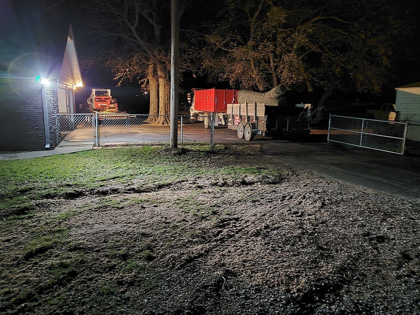 Nighttime outdoor yard with bright lights, a tent, red truck, and a metal fence beside a gravel area.