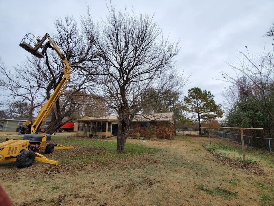 Yellow boom lift beside a house and leafless tree in a grassy yard